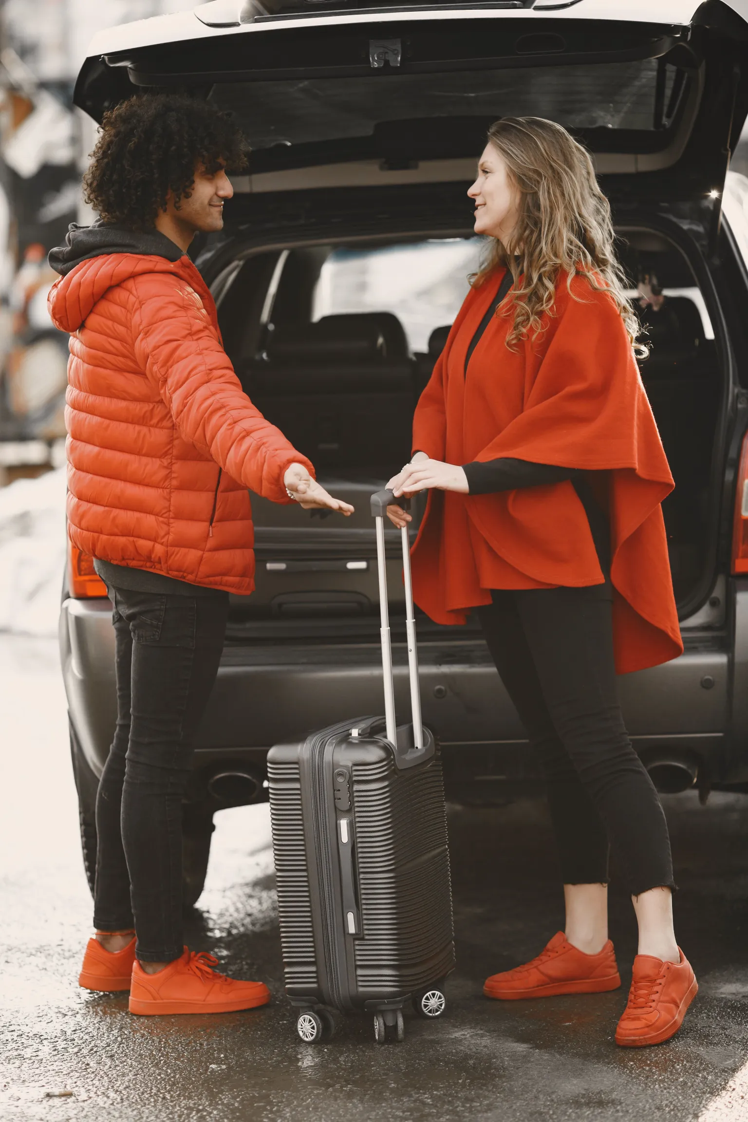 Couple with luggage beside the rear of a parked car.