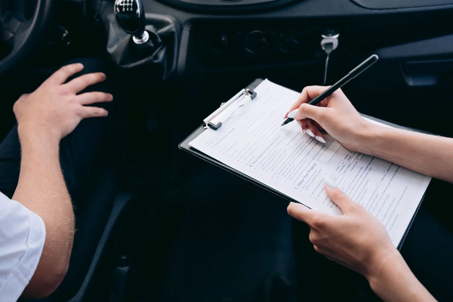 Hands holding a clipboard and writing inside a stationary car.